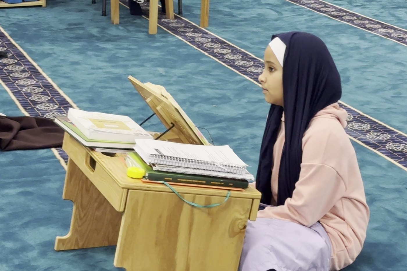 An Oceans Academy student reciting from her mushaf at a wooden rehl in the prayer hall